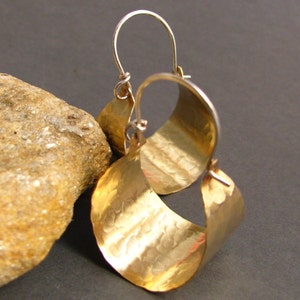 May include: A pair of gold hoop earrings with a hammered texture. The earrings are made of a thick, curved metal and have a simple, elegant design.