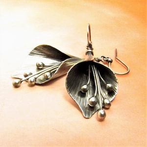 May include: Silver earrings with a flower design. The earrings are made of two silver leaves with a cluster of small silver beads hanging from the center.