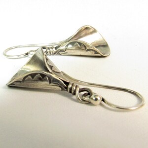 May include: A pair of silver earrings with a unique, textured, and slightly curved design. The earrings have a delicate, dangling style.