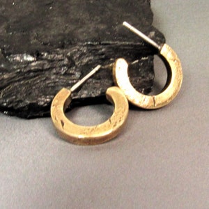 May include: A pair of gold hoop earrings with a textured finish. The earrings are made of metal and have a simple, minimalist design.