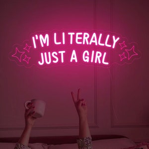 May include: Pink neon sign with the text "I'm literally just a girl" in a cloud shape with stars. The sign is hanging on a wall above a bed with pink bedding.
