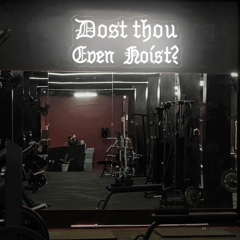 Puede incluir: Interior de un gimnasio con equipos de ejercicio y un espejo. Un letrero de ne&oacute;n sobre el espejo muestra el texto "Dost thou Even Hoist?" en una fuente g&oacute;tica. La habitaci&oacute;n tiene una est&eacute;tica oscura con tonos rojos y negros.