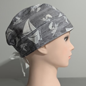 May include: Grey scrub hat with a white sailboat and fish print. The hat has a white tie.