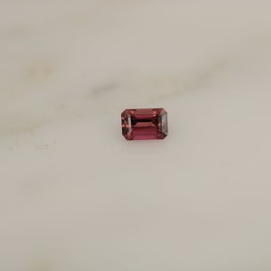 May include: A deep pink rectangular gemstone with a faceted cut.