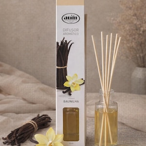 Può includere: Un diffusore di profumo alla vaniglia con una bottiglia di vetro trasparente, bastoncini di legno e una scatola con baccelli di vaniglia e un fiore giallo. La scatola recita "DIFUSOR AROMÁTICO" e "BAUNILHA".