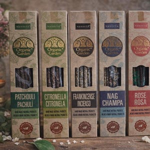 Peut inclure: Cinq boîtes d'encens Nandita Organic Garden, chacune étiquetée avec un parfum différent : Patchouli, Citronnelle, Frankincense, Nag Champa et Rose. Les boîtes sont marron avec des accents verts, bleus et rouges.