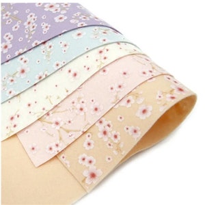 May include: A stack of six fabric sheets with a delicate floral pattern. The sheets are in shades of peach, pink, light blue, and lavender. The floral pattern features small white flowers with pink centres.