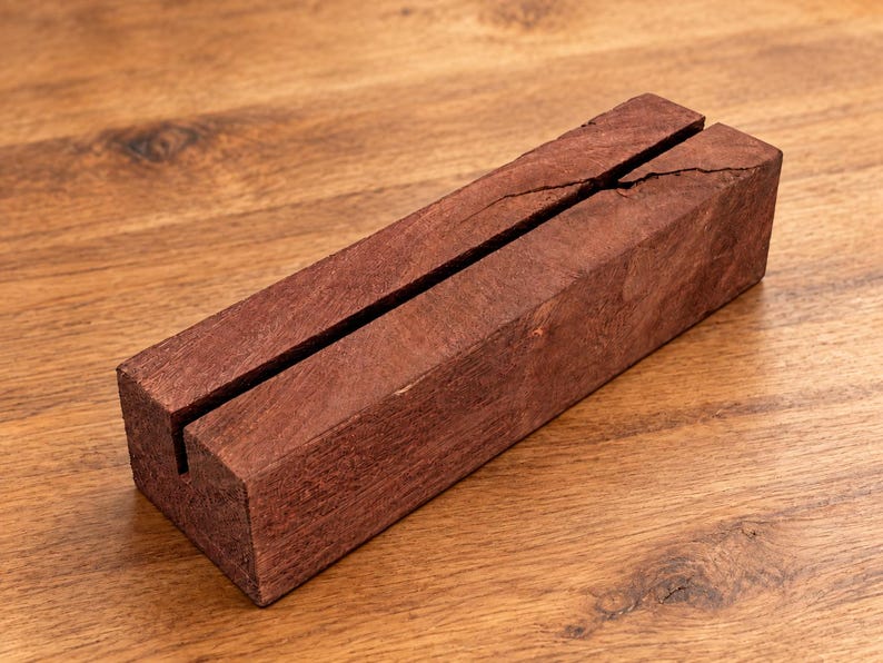 Puede incluir: Un bloque de madera rectangular de tono marr&oacute;n rojizo intenso con una veta visible. El bloque presenta una ranura vertical larga y estrecha a lo largo de la superficie superior, que tambi&eacute;n muestra una peque&ntilde;a grieta natural cerca del centro.