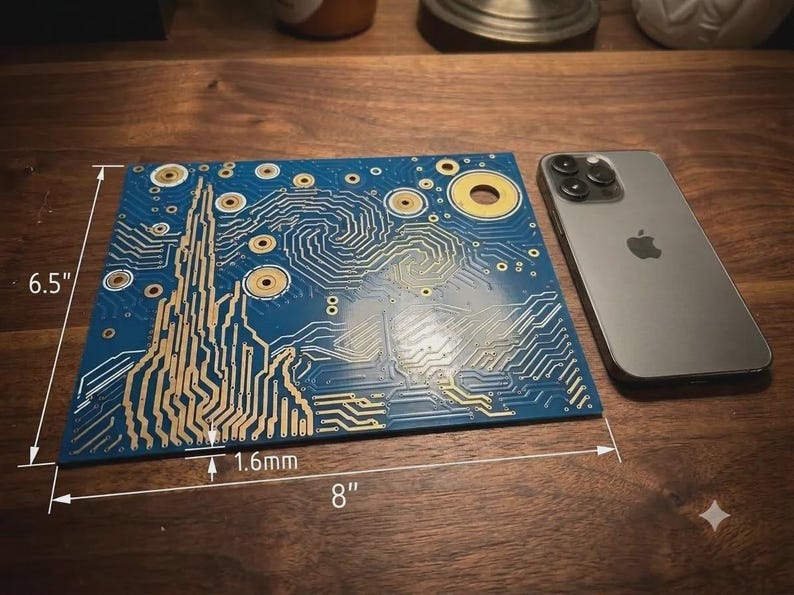 Puede incluir: Una placa de circuito impreso azul con un patr&oacute;n art&iacute;stico dorado de l&iacute;neas y c&iacute;rculos en espiral, que mide 16,51 cm por 20,32 cm con un grosor de 1,6 mm, junto a un tel&eacute;fono inteligente gris sobre una superficie de madera.