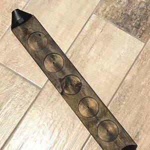 May include: A wooden coaster with six circular cutouts, designed to hold six glasses or mugs. The coaster has a dark brown stain and a black painted edge.