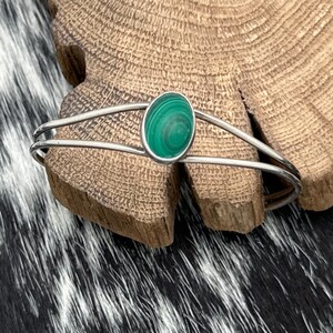 May include: A silver bangle bracelet with a green malachite stone set in the centre.