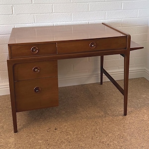 May include: A mid-century modern wooden desk with four drawers and a pull-out shelf. The desk has a light brown finish and round metal drawer pulls.