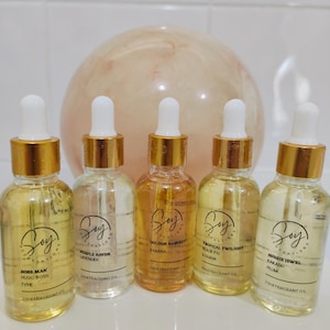 May include: Five 30 ml bottles of Soy Creations fragrant oil. The bottles are clear glass with gold lids and droppers. The labels are black with white text. The scents are Boss Man Hugo Boss Type, Purple Haven Lavender, Golden Harvest Banana, Tropical Twilight Black Fig & Guava, and Aussie Jewel Kakadu Plum.