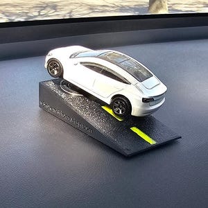May include: White toy car on a black ramp with a yellow line down the center. The car is a Tesla Model S.