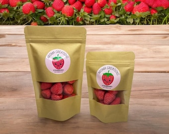 May include: Two brown paper bags with clear windows showing strawberry-scented soy wax melts inside. The bags have labels with the text "Aroma Creations" and a cartoon strawberry with a smiling face. The text on the label reads "Strawberry Soy Wax & Melt".