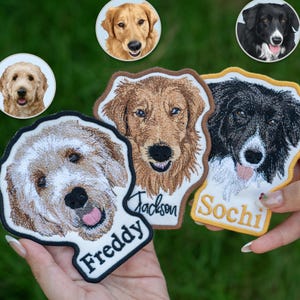 May include: Embroidered dog patches featuring detailed portraits of various dog breeds. The patches include names like "Freddy," "Jackson," and "Sochi." The patches have a white background with a black border and are held against a green background.