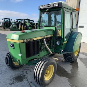 May include: A green John Deere 2855N tractor with a cab and a roll bar. The tractor is sitting on a concrete surface.