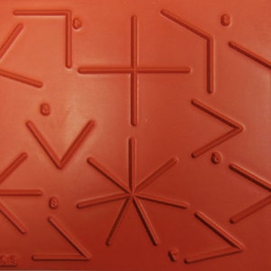 May include: A rectangular, orange silicone mold featuring various geometric shapes, including stars, angles, and crosses. The shapes are raised, creating a textured surface. The mold has text at the bottom.