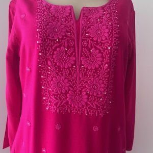 May include: A pink long-sleeved tunic with a floral embroidered neckline and sequins. The neckline is a V-shape and the sleeves are three-quarter length.