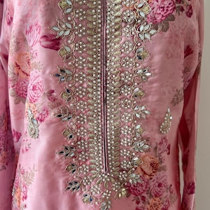 Puede incluir: Un kurta de estampado floral rosa con un escote decorativo adornado con perlas y espejos.