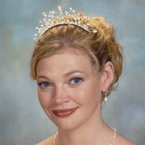 Puede incluir: Una mujer con una tiara plateada con detalles de cristal y pendientes de perla. Su cabello est&aacute; recogido en un mo&ntilde;o.