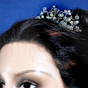 Puede incluir: Un peine de pelo plateado con cristales y perlas transparentes y blancas. El peine est&aacute; dise&ntilde;ado con un delicado patr&oacute;n de vid.