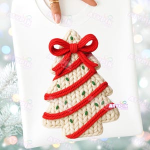 May include: White sweatshirt featuring a Christmas tree design. The tree is cream-colored with red accents, including a bow at the top and stripes. Small green dots are scattered across the tree, adding a festive touch. The sweatshirt is a cozy holiday apparel item.