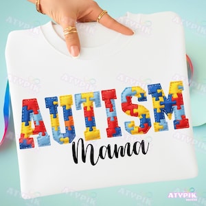 May include: White sweatshirt with the word "AUTISM" in colorful puzzle piece letters and the word "Mama" in black script. The sweatshirt is a crew neck style.