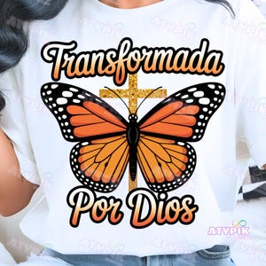 May include: White t-shirt with a monarch butterfly design. The butterfly has orange and black wings, a gold cross, and the text "Transformada Por Dios" in black and orange. The design is centered on the shirt.