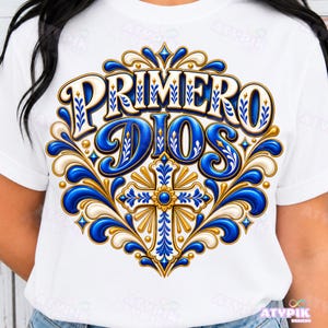 Könnte beinhalten: Ein weißes T-Shirt mit einem großen, verzierten Grafikdesign in Blau-, Gold- und Weißtönen. Der Text "PRIMERO DIOS" ist in fetter, stilisierter Schrift über einem zentralen Kreuzmotiv zu sehen, das von verschlungenen Blumenmustern umgeben ist.