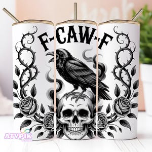 May include: White tumbler featuring a black raven on a skull, framed by roses and thorny vines. The text "F-CAW-F" is above the raven. Includes a gold-coloured straw.