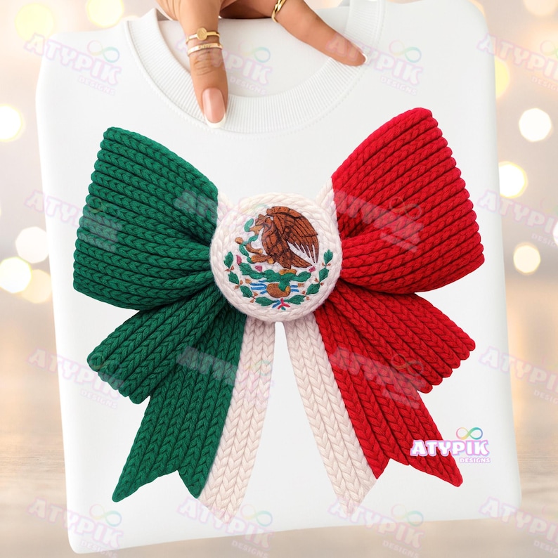 May include: White sweatshirt with a large bow design in the colours of the Mexican flag: green, white, and red. The bow has a central emblem with the Mexican coat of arms. The design is made of a knitted material.