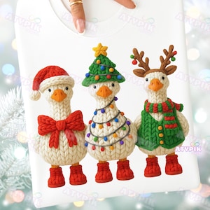 May include: White sweatshirt featuring three geese dressed for Christmas. One goose wears a Santa hat and bow, another a Christmas tree, and the third a reindeer costume. Each goose has red boots. The text "ATYPIK" is visible.
