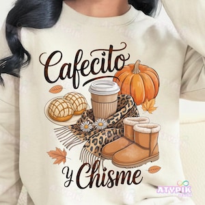 May include: Beige sweatshirt with a fall-themed graphic. The design includes a coffee cup, pumpkin, bread, scarf, and boots. Text reads "Cafecito y Chisme". The design has a cozy, autumn aesthetic.