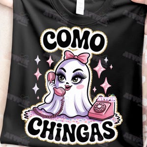 May include: Black t-shirt with a cartoon ghost wearing a pink bow, holding a pink telephone. The text "COMO CHINGAS" is above and below the ghost illustration, with pink star accents.