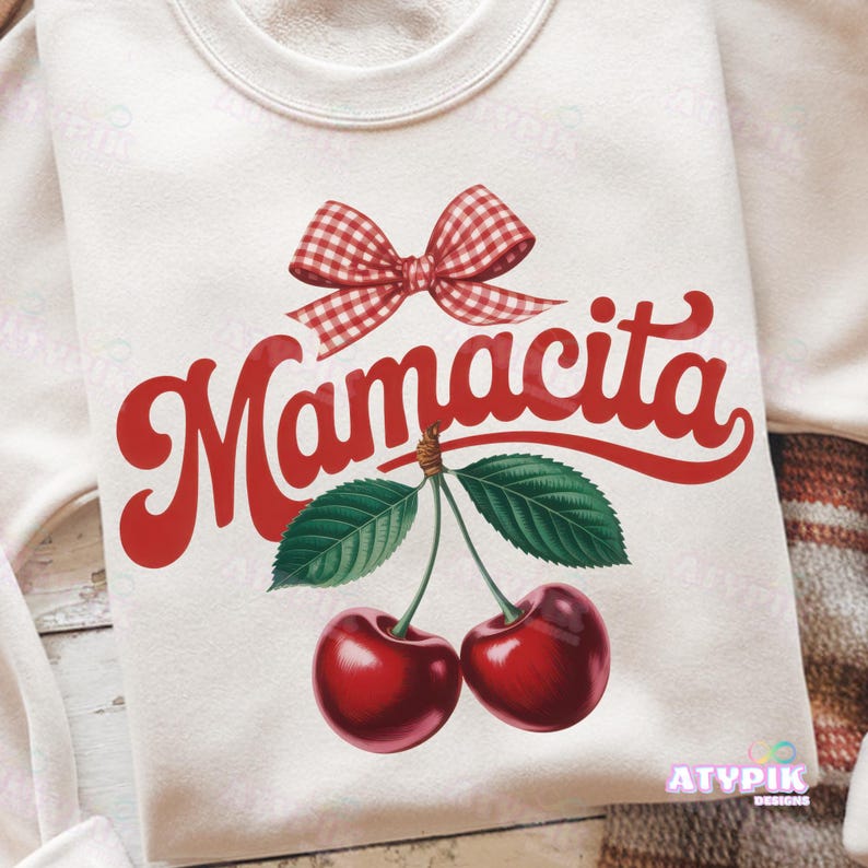 K&ouml;nnte beinhalten: Cremefarbenes Sweatshirt mit einer roten Vichy-Schleife und dem Wort "Mamacita" in roter Schrift. Darunter zwei Kirschen mit gr&uuml;nen Bl&auml;ttern. Das Design hat eine Vintage- und Retro-&Auml;sthetik.