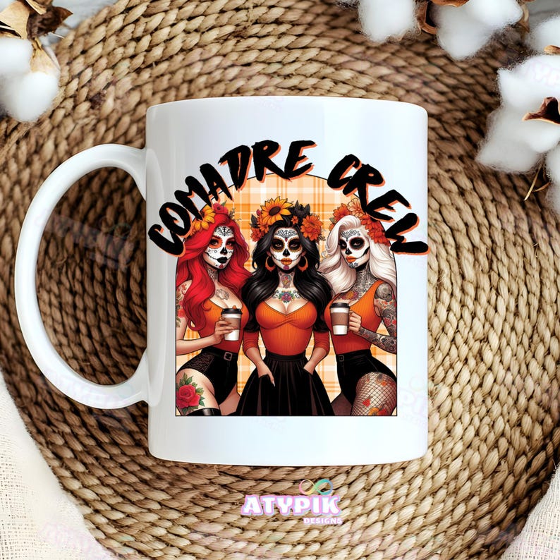 May include: White ceramic coffee mug with a black and orange design featuring three women with sugar skulls and the text "Comadre Crew".