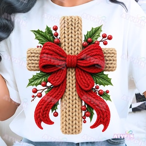 May include: A white t-shirt featuring a graphic of a tan, cable-knit textured cross. The cross is adorned with a large, bright red, thick-textured bow at the centre, surrounded by green holly leaves and clusters of small, round red berries.
