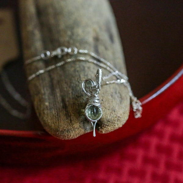 Sparkly faceted green peridot with tiny, round pale blue topaz accent, wrapped in sterling silver