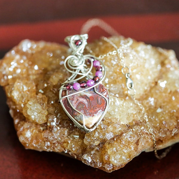 Crazy Lace Agate Heart wrapped in .940 Argentium Silver wire with clip chain included. Adorned with small garnets and rubies.