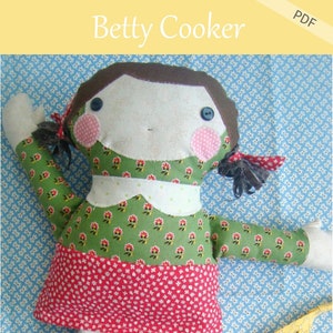 Puede incluir: Muñeca de tela hecha a mano llamada "Betty Cooker" con un vestido floral verde y una falda roja. La muñeca tiene cabello castaño, mejillas rosadas y ojos azules de botón. La imagen incluye el texto "Patchwork Posse" y "PDF".