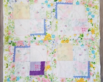 Può includere: Una trapunta patchwork con motivi floreali. È composta da quadrati di tessuto in vari colori, tra cui bianco, rosa, giallo, blu e viola. Alcuni quadrati hanno bordi in pizzo. I bordi sono rifiniti con un bordo floreale.