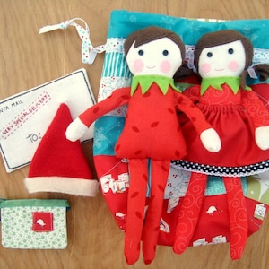 Peut inclure: Poupées elfes de Noël faites à la main, vêtues de rouge et de colliers verts, à côté d'une chaussette patchwork. Comprend un bonnet de Père Noël, un petit sac cadeau et une enveloppe en feutre avec le texte "Santa Mail".