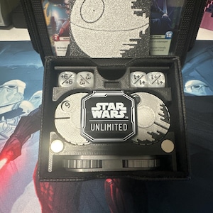Könnte beinhalten: Ein schwarzer Star Wars Unlimited-Spielkoffer mit einem Death-Star-Design. Der Koffer verfügt über ein Fach für Würfel und Karten. Der Koffer trägt das Star Wars Unlimited-Logo auf der Vorderseite.