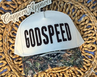 Puede incluir: Una gorra de béisbol blanca con la palabra GODSPEED bordada en letras marrón oscuro en el panel frontal. La visera tiene un patrón de camuflaje y una pegatina con el texto D&Y David Jay Young. La marca Cappora Apparel es visible.