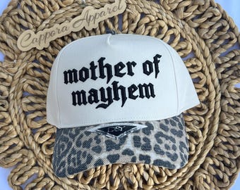 Puede incluir: Una gorra de béisbol de color crema con el texto bordado en negro mother of mayhem en el panel frontal. La visera presenta un estampado de leopardo gris y negro con una pequeña pegatina de D&Y David & Young centrada en la visera.