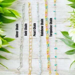 May include: Five distinct bracelets arranged vertically: a silver chain, a gold chain, a pearl chain, a rainbow chain with multi-colored links, and a turquoise chain with small blue stones. Each bracelet features a metal clasp at the top end.