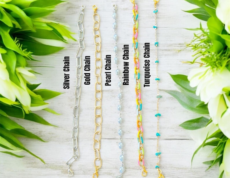 May include: Five distinct bracelets arranged vertically: a silver chain, a gold chain, a pearl chain, a rainbow chain with multi-colored links, and a turquoise chain with small blue stones. Each bracelet features a metal clasp at the top end.