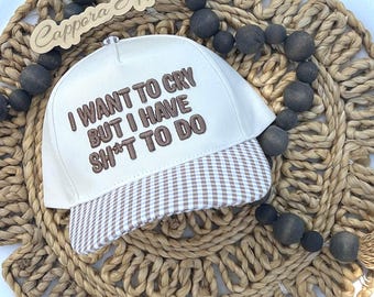 Puede incluir: Una gorra de béisbol blanca con visera de cuadros vichy marrones y texto bordado en marrón que dice I WANT TO CRY BUT I HAVE SH*T TO DO. La gorra presenta una corona estructurada y un botón en la parte superior con un diseño claro.