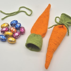 Könnte beinhalten: Zwei gestrickte Osterkörbe in Karottenform mit grünen Oberteilen. Die Körbe sind gefüllt mit bunten, in Folie verpackten Schokoladeneiern.